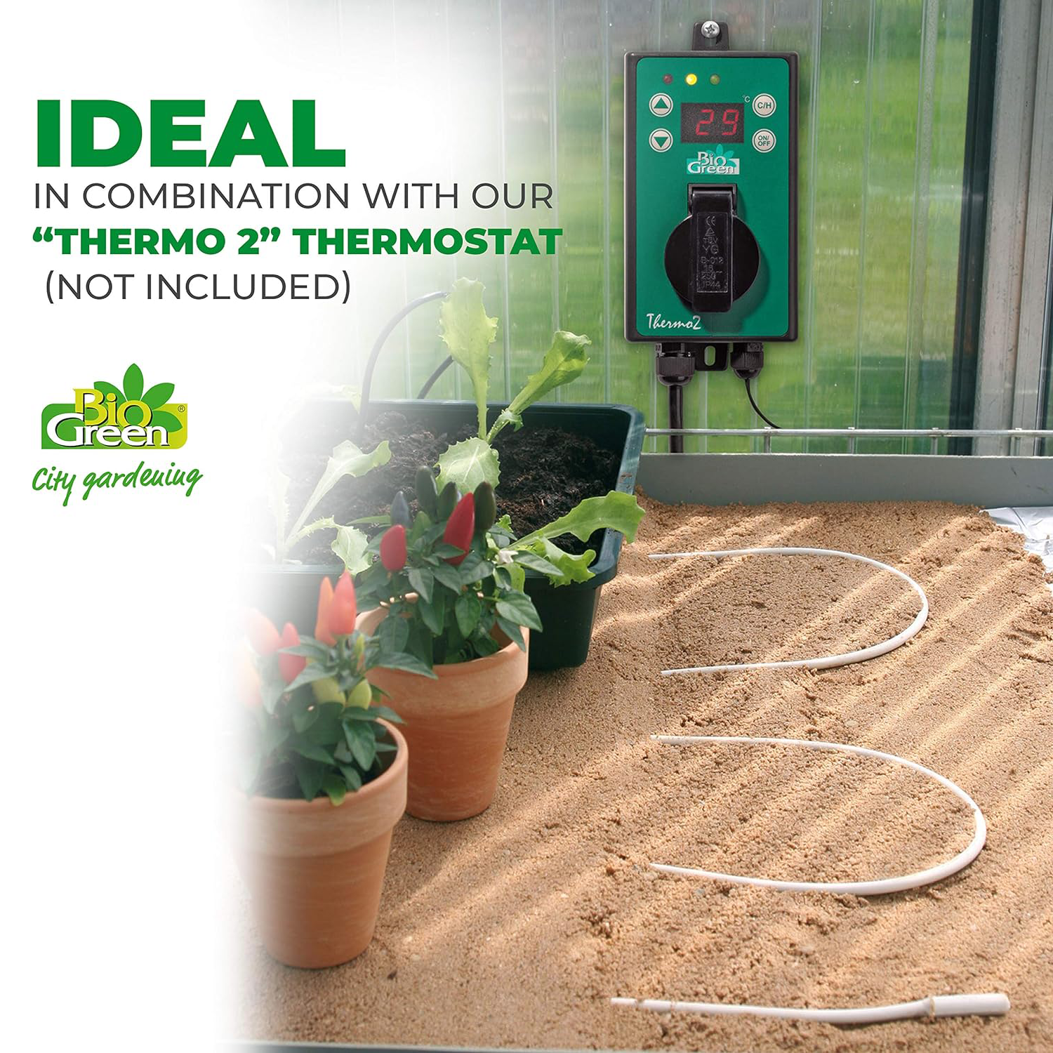 The image shows a flexible heating cable laid across the soil in a greenhouse with potted plants on top. The cable is connected to a "THERMO 2" thermostat (which is not included in the image) and is ideal for use with it to regulate the soil temperature for plant growth. The image emphasizes that the thermostat is not included with the heating cable.